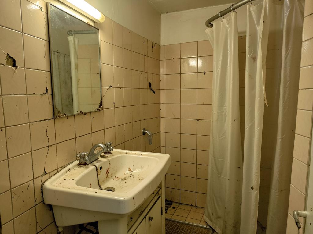 Slitet badrum före renovering med gammalt kakel och sliten inredning