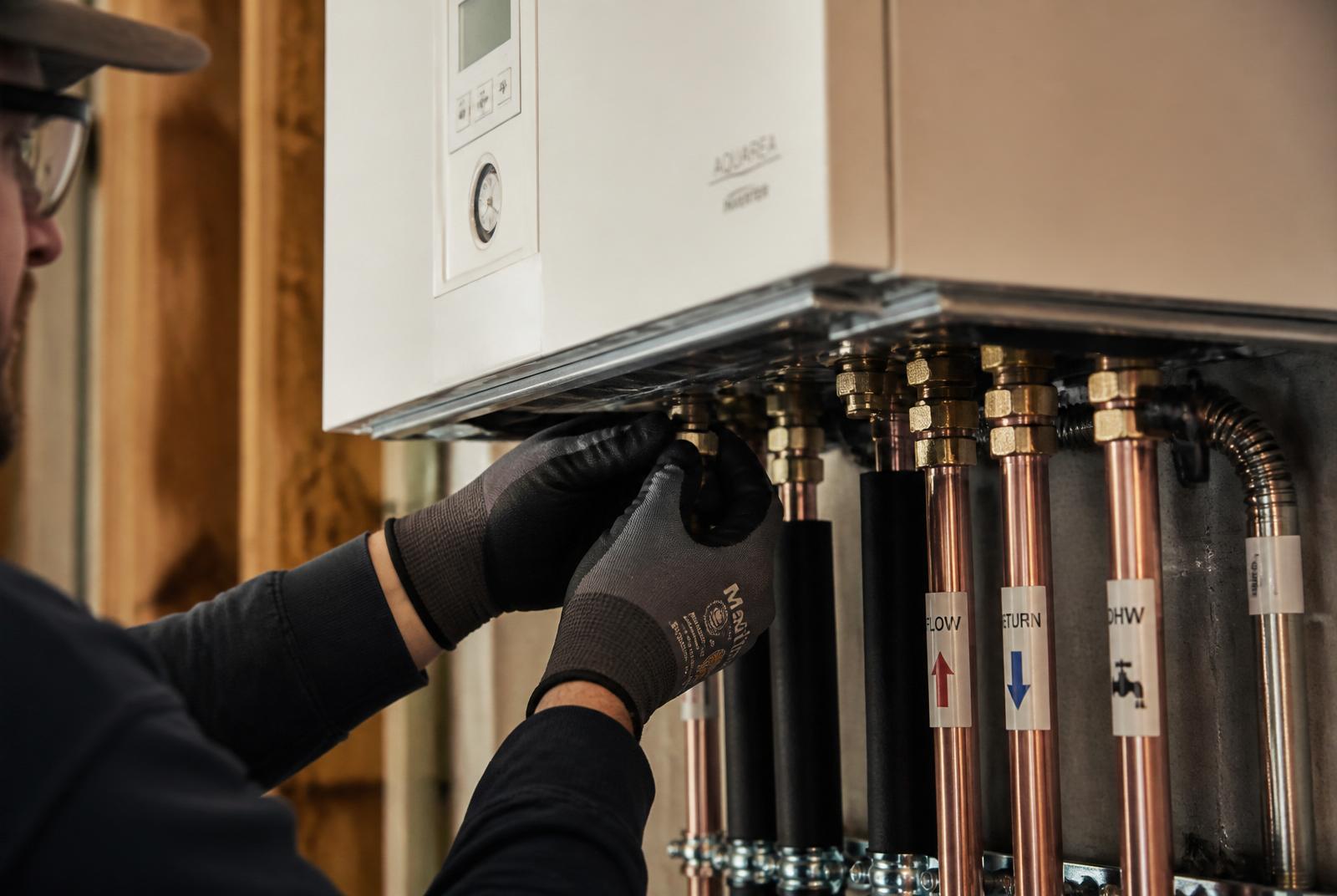 Närbild på montörens händer som installerar en modern väggmonterad värmepump med raka, isolerade kopparrör och tydligt märkta flödesledningar